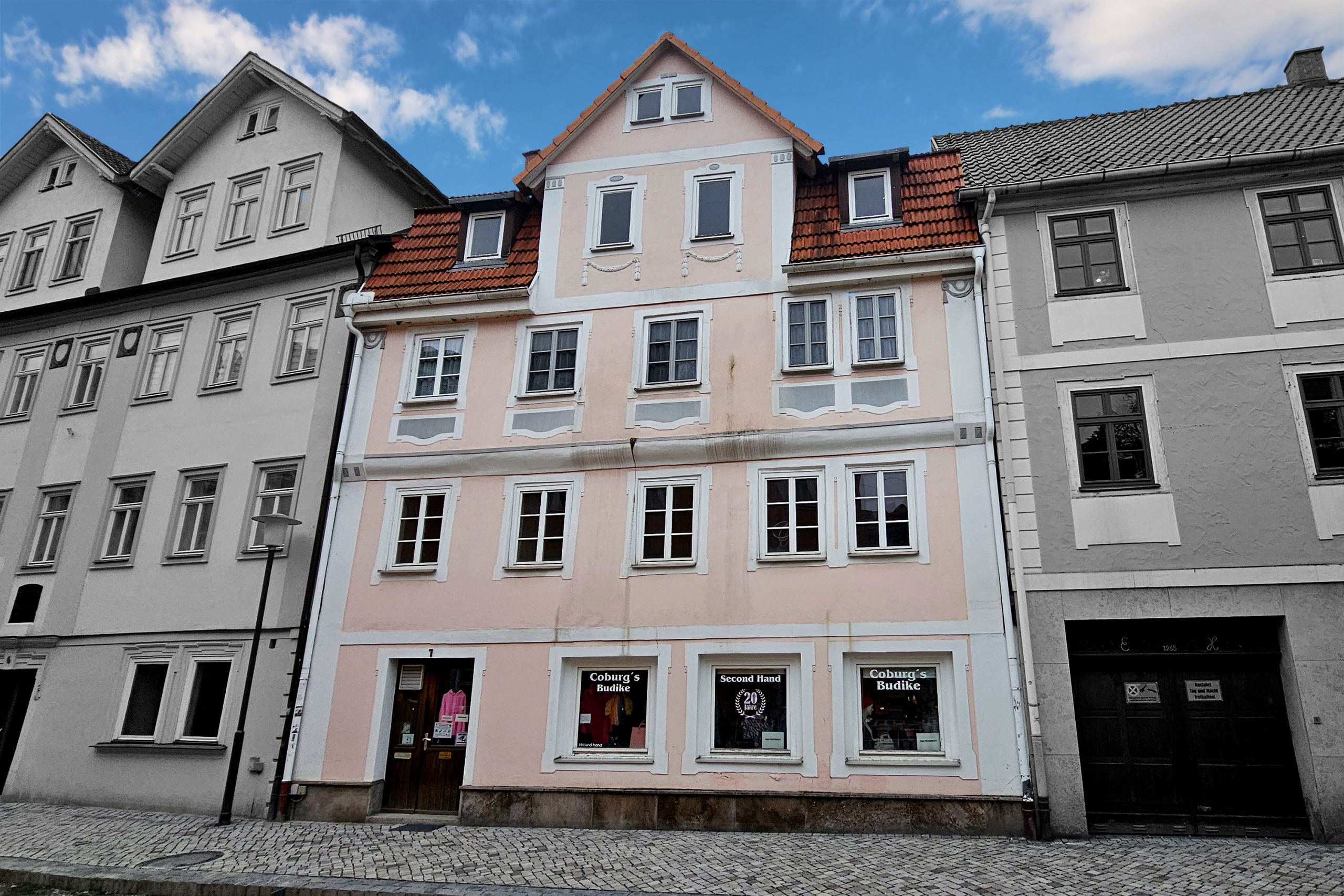 BA 73 Fassade Drei mehrstöckige Stadthäuser in einer gepflasterten Straße; das mittlere Haus ist farbig hervorgehoben.