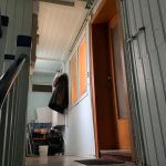 Blick von einer Treppe in einen hellen Flur mit Holztüren, weißen Paneel-Wänden und einer Garderobe.