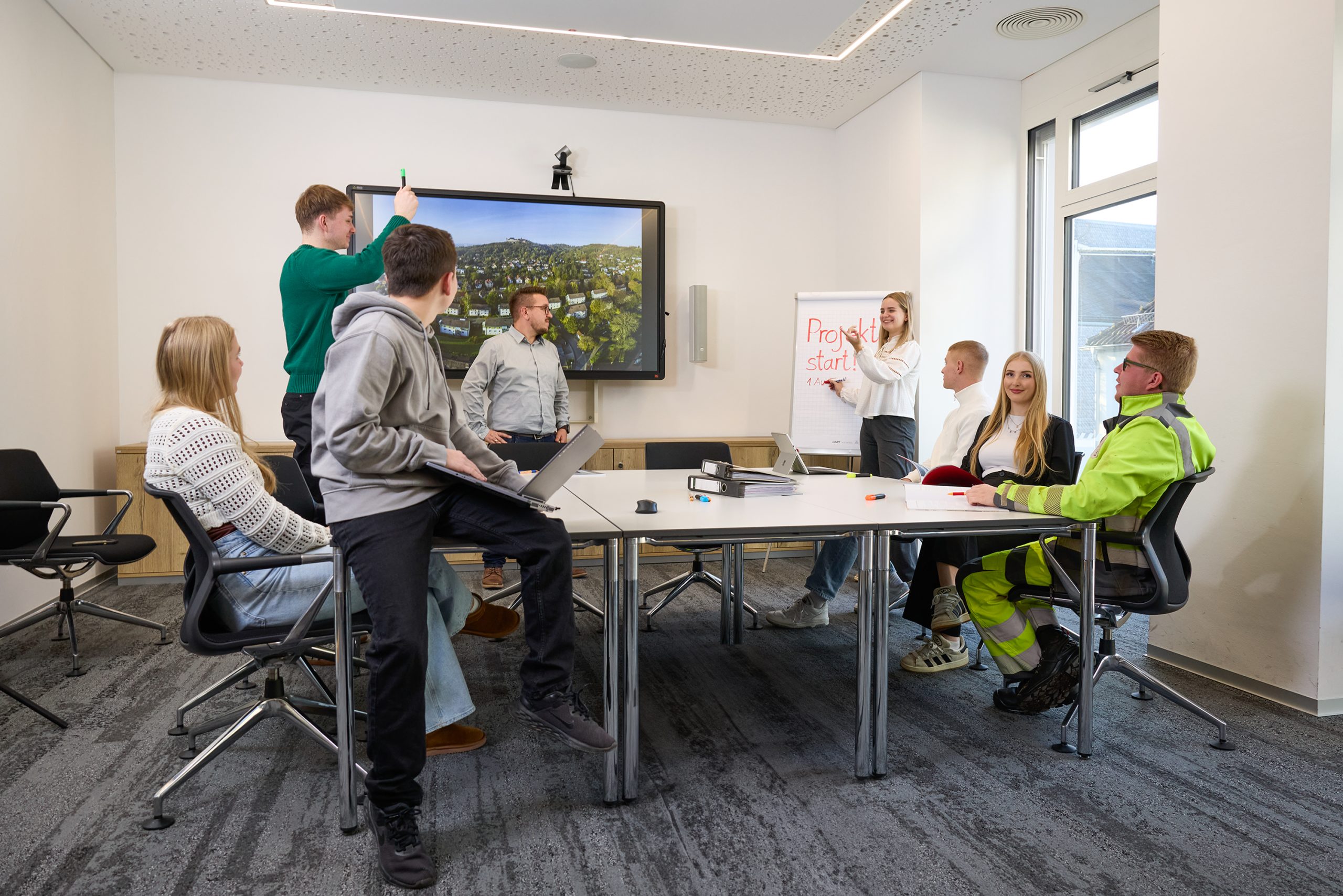 Ausbildung in Coburg Gruppe junger Menschen in einem modernen Besprechungsraum bei einer Projektbesprechung mit Präsentation am Bildschirm und Flipchart.