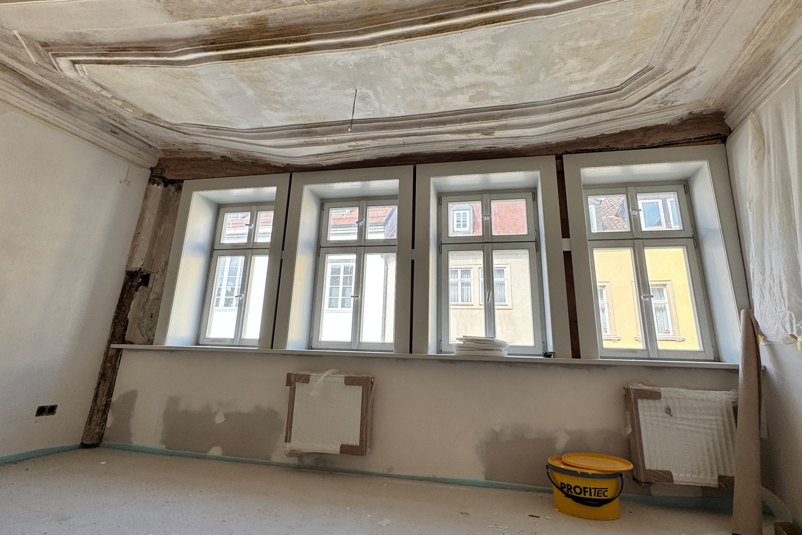 Raum im Baustellenzustand mit abgeklebten Heizkörpern und einer Stuckdecke.