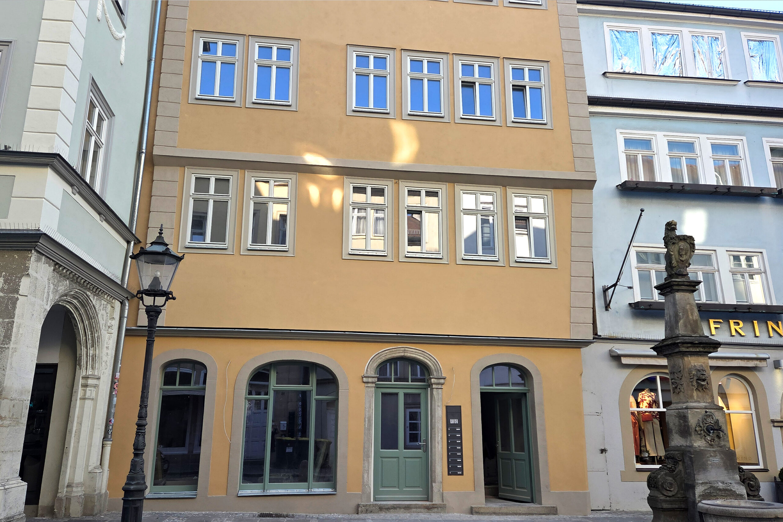 Gebäude mit gelber Fassade und grüner Tür und Brunnen vor dem Gebäude.