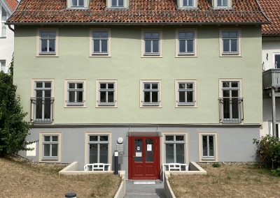 Außenansicht eines hellgrünen Gebäudes mit roter Tür.