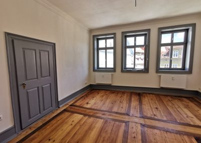 Innenraum mit Holzboden, grauen Fenstern, einer grauen Tür und grauen Sockelleisten.