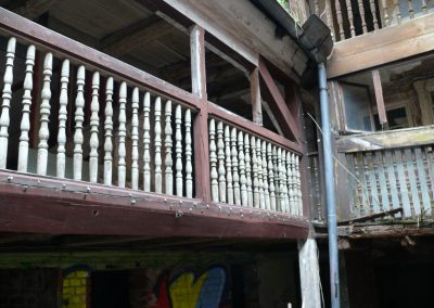 Detailaufnahme eines alten, dunkelbraunen Laubengangs aus Holz mit weiß gestrichenen, gedrechselten Geländerstäben.