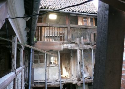 Blick in einen baufälligen Innenhof. Ein hölzerner Laubengang mit gedrechseltem Geländer im Obergeschoss wird im Erdgeschoss durch zahlreiche Metallbaustützen abgesichert.