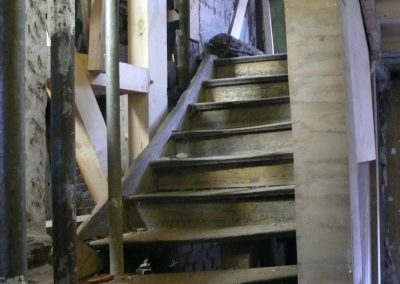 Eine baufällige Holztreppe während der Sanierung, umgeben von massiven Holz- und Metallstützen.