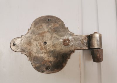 Detailaufnahme eines alten Metallenen Türscharniers auf einer weißen Tür.