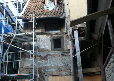 Baustelle im engen Innenhof mit einem aufgebauten Metallgerüst an einer freigelegten, alten Fachwerk- und Putzwand.