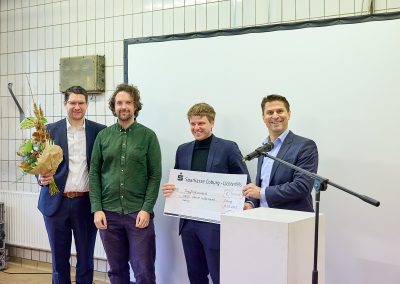 Vier Personen mit Blumenstrauß und Scheck
