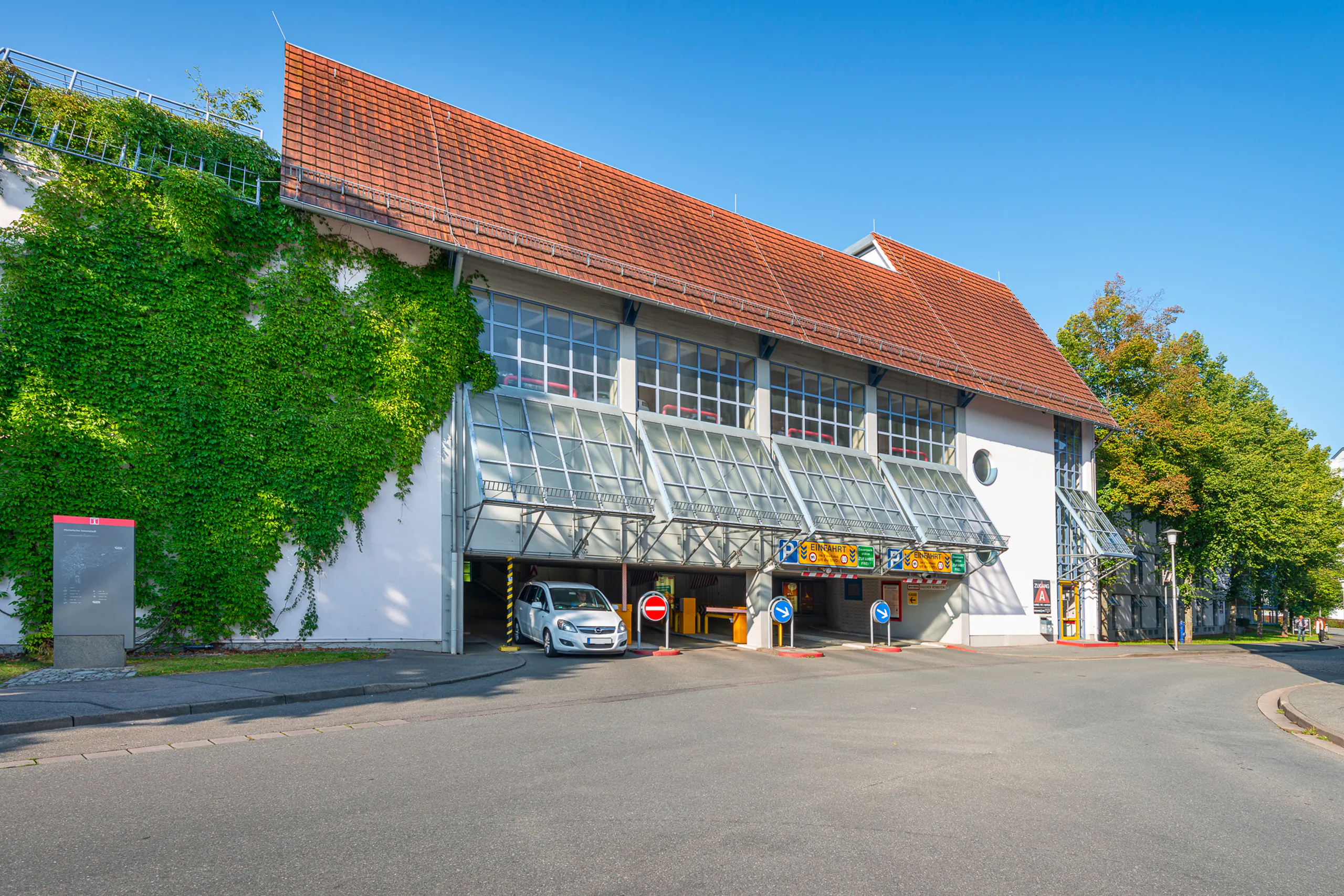Außenansicht eines Parkhauses mit sichtbarer Ein- und Ausfahrt. Die Fassade ist begrünt.
